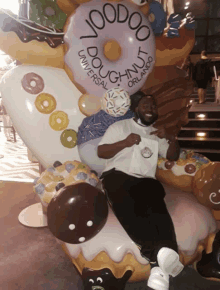 a man sits in front of a giant donut that says voodoo doughnut universal orlando