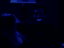 a man and a woman are sitting under a lamp in a dark room . the man is glowing in the dark .