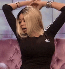 a woman is sitting on a pink couch with her arms outstretched and wearing a black adidas shirt .