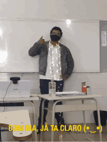 a man wearing a mask is standing in front of a white board with the words bom dia ja ta claro