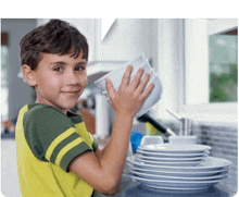 a young boy in a yellow shirt is washing dishes