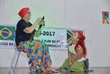 a woman sits in a chair next to a woman kneeling in front of a sign that says " 2017 "