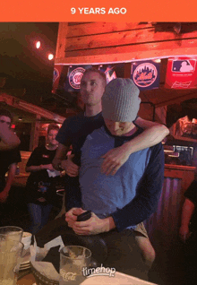 two men hugging in a bar with a sign that says timehop