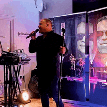 a man singing into a microphone in front of a wall with a picture of a man on it