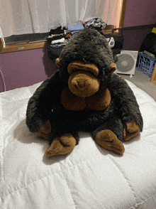 a stuffed gorilla sits on a bed in front of a fan