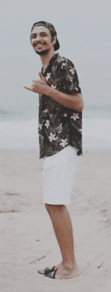 a man in a floral shirt and white shorts stands on the beach