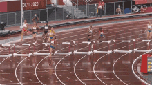 a group of women are running hurdles on a track with a sign that says tokyo 2020 in the background