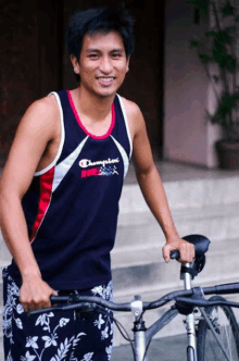 a man wearing a champion tank top holds a bicycle