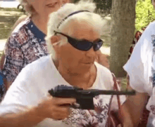 an older woman wearing sunglasses is holding a gun in her hand .