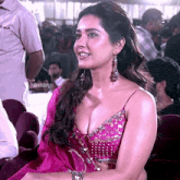 a woman wearing a pink top and earrings is sitting in front of a sign that says devasena
