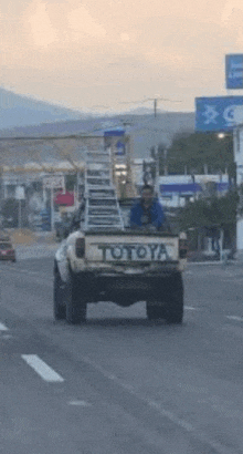 a man is driving a toyota truck with a ladder in the bed .