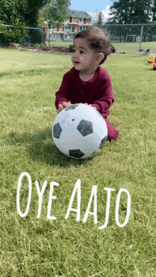 a baby is sitting on the grass holding a soccer ball with the words oye aajo written on the grass