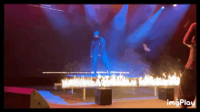 a man in a blue hoodie is standing on a stage with flames coming out of it and the words imgplay below him