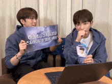 two young men sitting at a table holding signs one of which says " i love you " in chinese