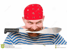 a man with a red bandana and a beard is holding a large knife in his mouth