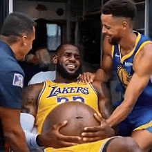 a basketball player is holding his pregnant belly while being helped by two other basketball players .