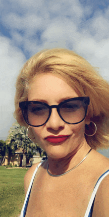 a woman wearing sunglasses and hoop earrings stands in front of palm trees