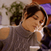a woman wearing a grey sweater is holding a glass of milk