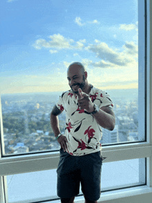 a man in a floral shirt is standing in front of a window and giving a thumbs up