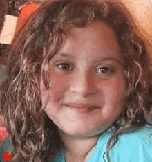 a little girl with curly hair is smiling at the camera .