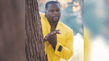 a man in a yellow suit is peeking around a tree