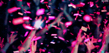 a crowd of people raising their hands in the air with confetti falling from the sky