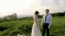 a bride and groom are standing in a grassy field . the bride is touching the groom 's arm .