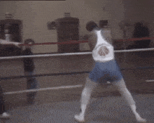 a man stands in a boxing ring watching a man in a white shirt with a red circle on the back