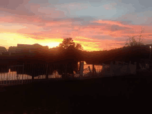 a sunset over a lake with a white fence