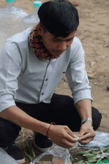 a man in a white shirt and black pants is kneeling down with a bag of green beans in front of him