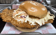 a chicken sandwich with coleslaw on a bun in a styrofoam container