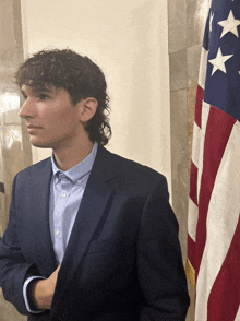 a man in a suit stands in front of a flag