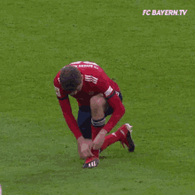 a soccer player is tying his shoes on a field with fc bayern.tv written on the bottom of the screen