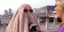 a woman covering her face with a blanket is being interviewed by a local 7 news reporter