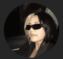 a woman wearing sunglasses and a black jacket looks at the camera