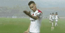 a man in a white shirt is standing on a soccer field with his hand up .