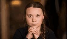 a close up of a young woman with her hands folded looking at the camera .