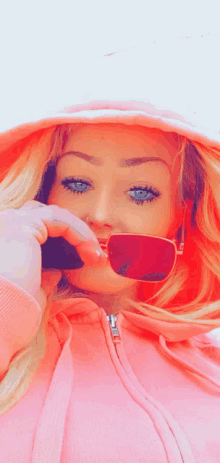 a woman wearing a pink hoodie and red sunglasses takes a selfie