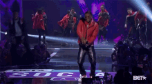 a man in an orange jacket is dancing on a stage in front of a bet logo