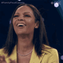 a woman in a yellow jacket is laughing with the hashtag familyfeudcanada