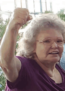 a woman wearing glasses and a purple shirt is holding her fist up in the air