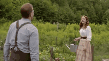 a man and a woman are standing next to each other in a garden . the woman is holding a watering can .