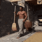 a shirtless man is holding a broom in front of a stone wall and a sign that says por 10