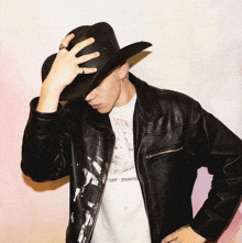 a man wearing a cowboy hat and a leather jacket holds his hand to his head