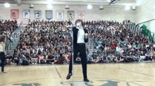 a man is singing into a microphone in front of a crowd in a gym with banners on the wall that say warrior