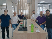 a group of men sitting around a table with one wearing a purple shirt that says uni