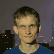 a young man in a blue shirt is smiling for the camera in front of a city skyline .