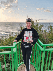 a woman wearing a black mad max shirt stands on a green railing