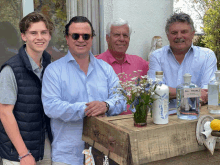 a group of men standing next to a wooden box with a bottle of gin on it