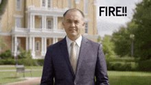 a man in a suit and tie stands in front of a building with the words fire written on the bottom